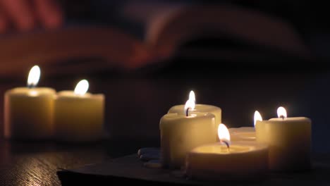 las manos del hombre siguen las líneas de un libro mientras están iluminadas por velas 4k