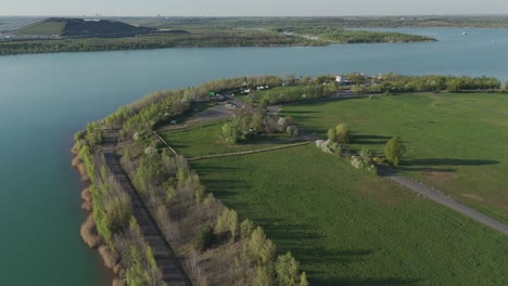 aerial view of störmthaler see near leipzig in late afternoon. calm lake, beach, road and spring trees in a straight forward drone shot with long shadows and clear sky.