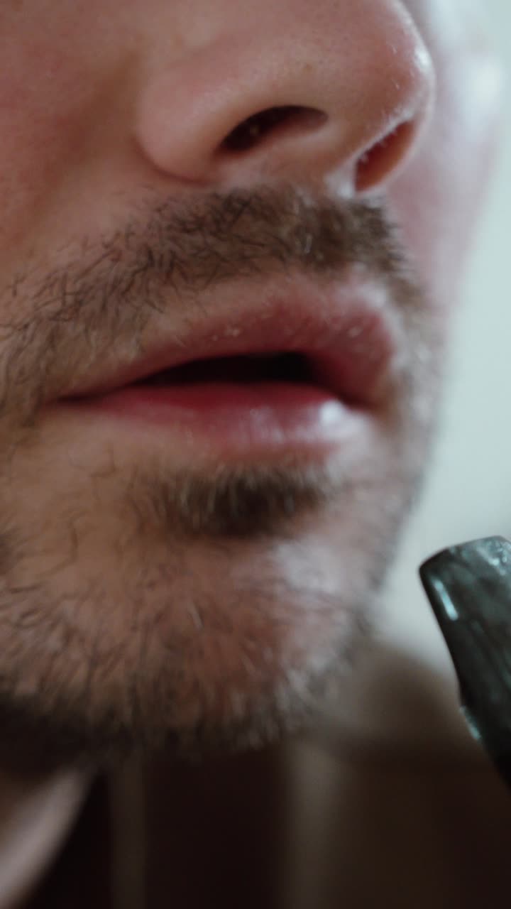 Extremnahe Aufnahme eines bärtigen Mannes, der eine E-Zigarette benutzt und Dampf ausatmet, mit Fokus auf trockene Lippen, Gesichtsbehaarung, Munddetails und realistische Alltagsstruktur in einer vertikalen Makroaufnahme.