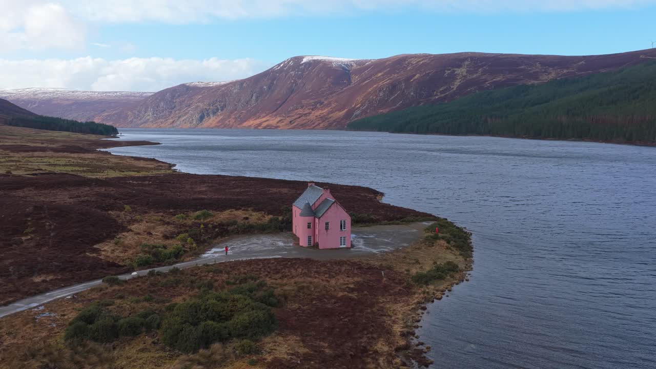 Lyserødt hus ved bredden af Loch Glass i de skotske højlande.
