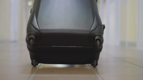 small wheels of big black suitcase spin on tile floor