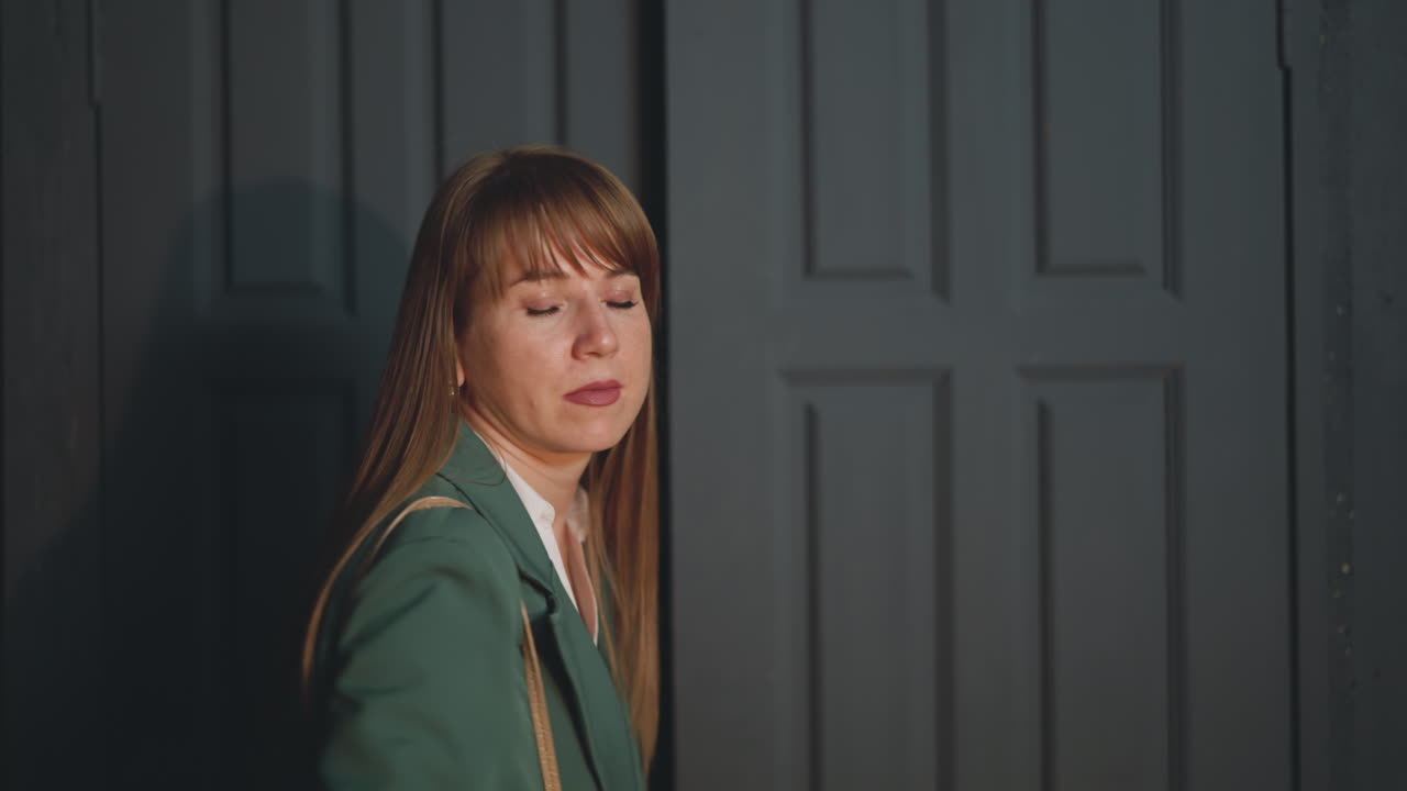 똑바로 빨간 머리카락을 가진 피곤한 여성이 저녁에 집에 들어갑니다.