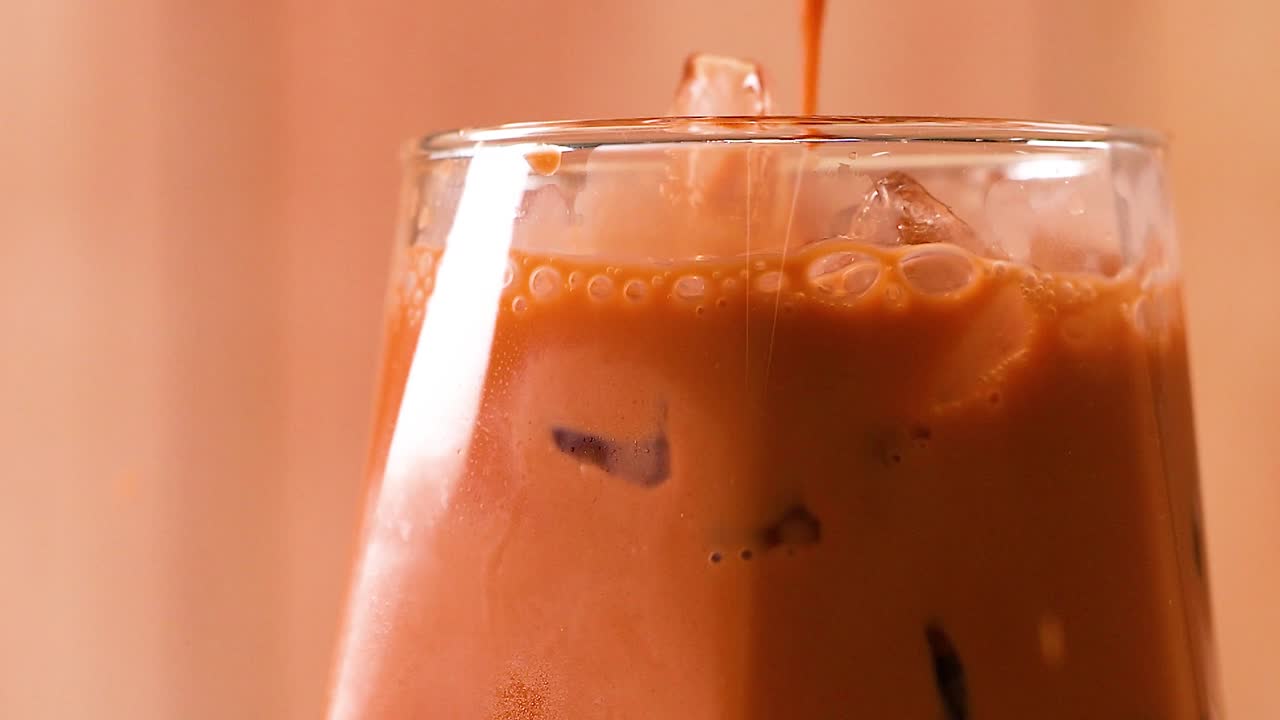 Una macro ravvicinata di tè al latte arancione versato in un bicchiere con ghiaccio.