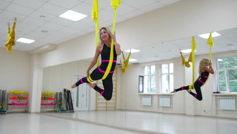 young beautiful woman doing aerial yoga practice in purple hammock in fitness club.