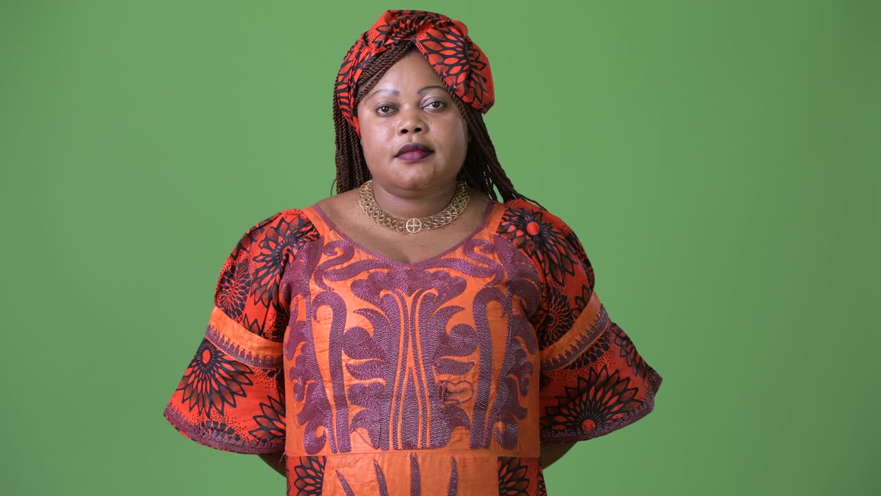 Overweight beautiful African woman wearing traditional clothing against green background