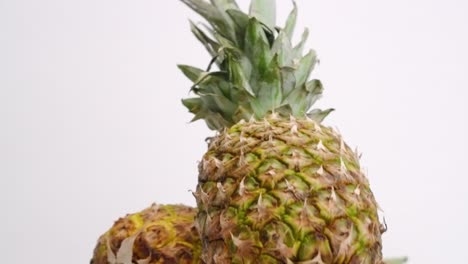 two whole yellow pineapples falling and bouncing into each other on white backdrop in slow motion