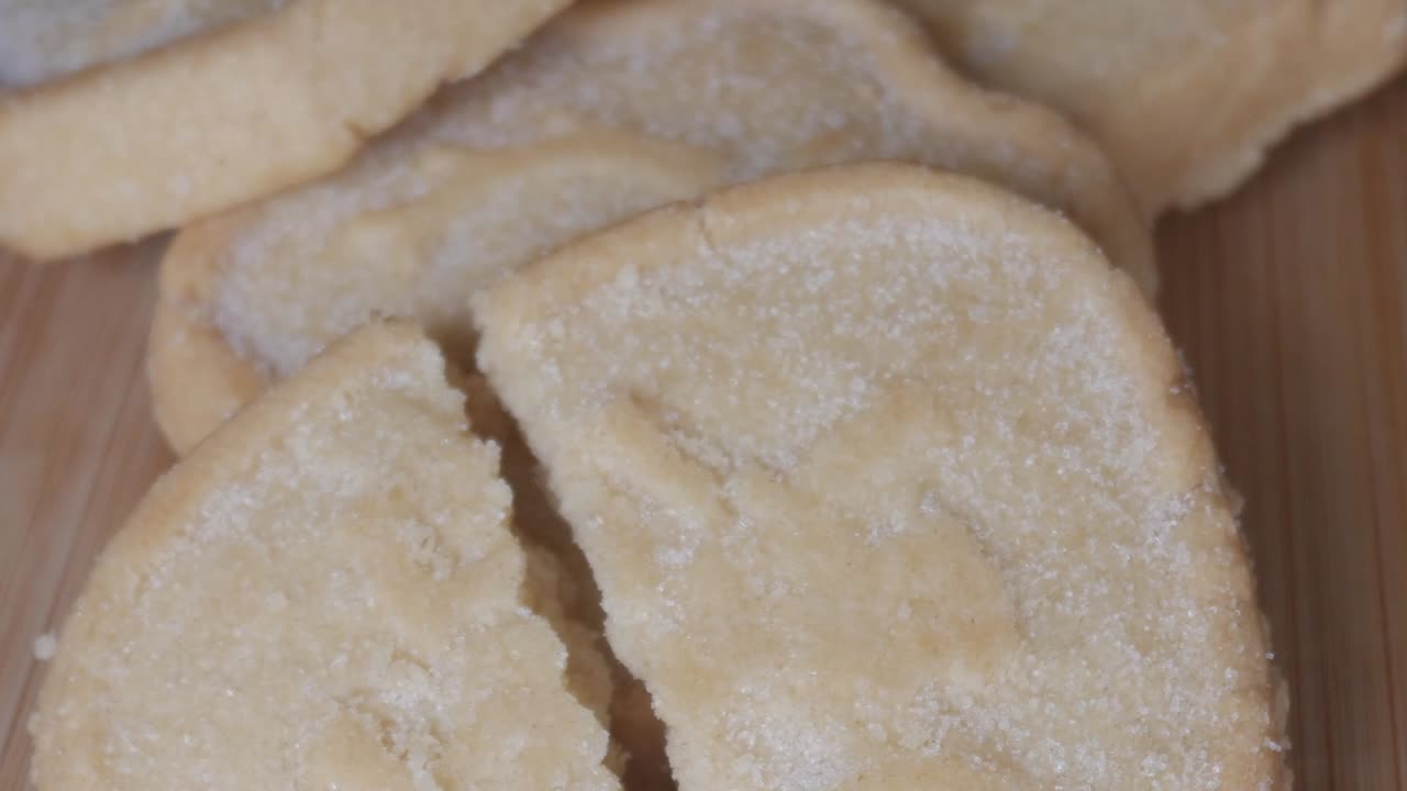 Round shortbread cookie cracked in half on wooden board, sugar coating visible on the surface