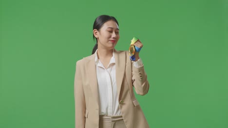 asian business woman in a suit looking at a gold medal then screaming goal celebrating winning as the first winner on green screen background in the studio