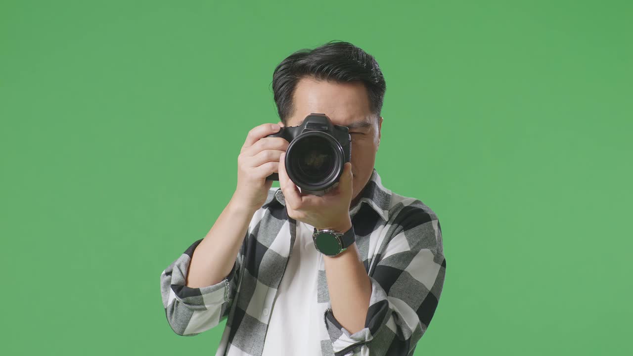 스튜디오에서 녹색 스크린 배경에 서서 사진을 찍고 미소 짓는 카메라를 사용하는 아시아 사진작가의 클로즈업