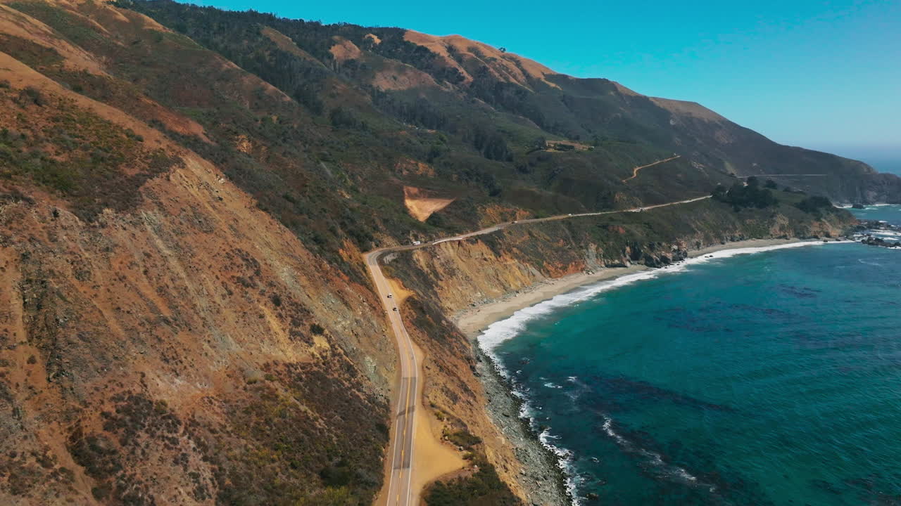 Road along the sloping mountainous coast of Pacific in California. Amazing scenery of the shoreline on sunny hot day. Top view.