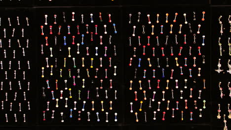 una colección de metales y coloridos piercings corporales está ordenadamente dispuesta en filas en una pantalla negra