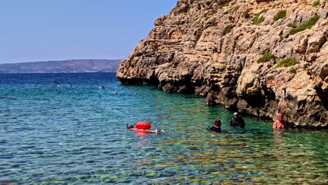 snorkelers exploring crystal-clear waters near a rocky coastline on a sunny day with vibrant blue sea