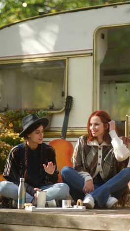 two women relaxing by a camper in autumn