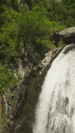 waterfall with foamy splashes runs down from rock ledge in summer forest. whitewater river cascade on high cliff in reserved park. hiking time