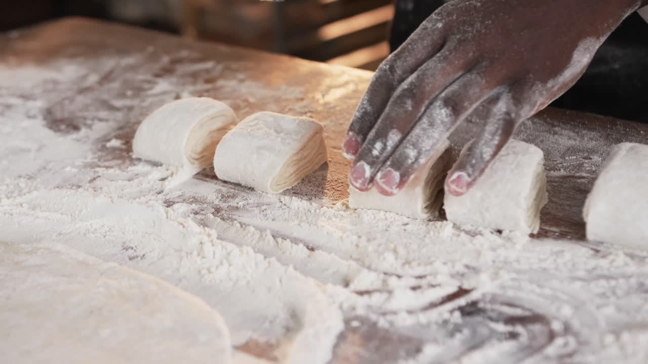 African american male baker working in bakery kitchen, cutting dough on counter in slow motion