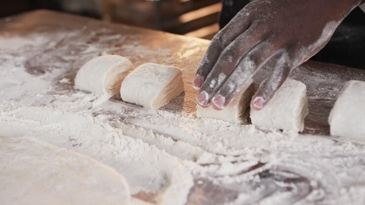 African american male baker working in bakery kitchen, cutting dough on counter in slow motion