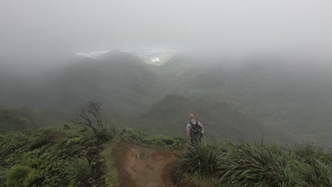 Camera-follows-young-male-hiker-on-steep-mountain-ridge-trail,-Hawaii