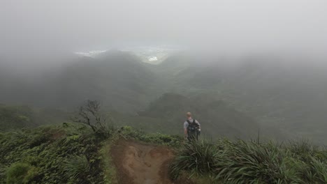 camera follows young male hiker on steep mountain ridge trail, hawaii