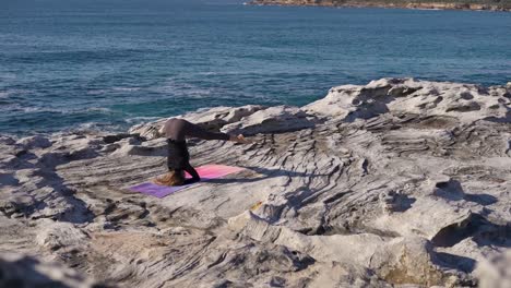 mujer haciendo yoga en un acantilado del océano al amanecer