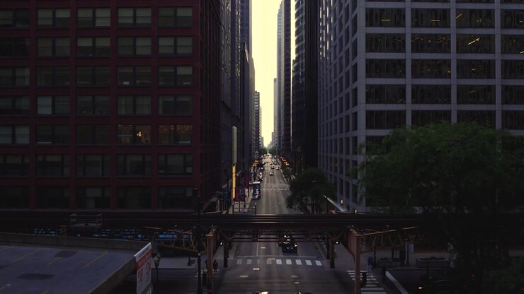 Vista drone su una strada del centro di Chicago incorniciata da grattacieli, traffico e binari sopraelevati della CTA durante la calda luce serale.