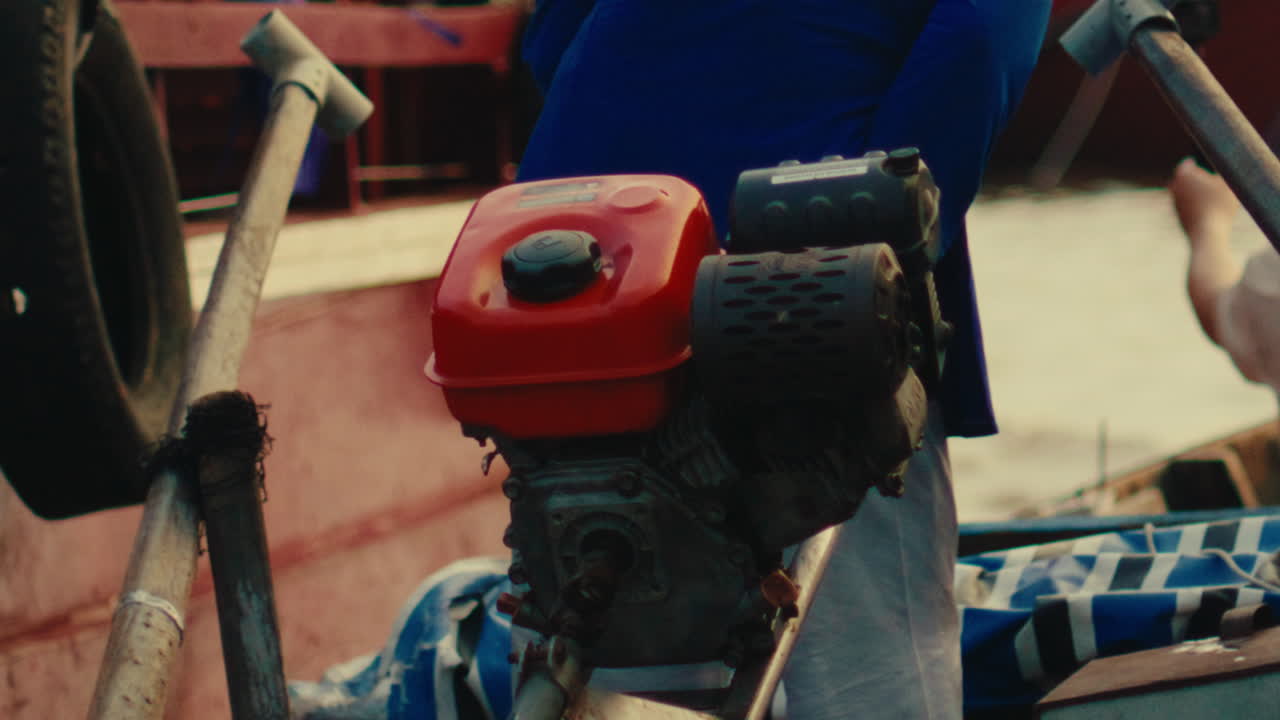 Boat engine with red cover on a wooden boat in Vietnam, operated by a person in blue