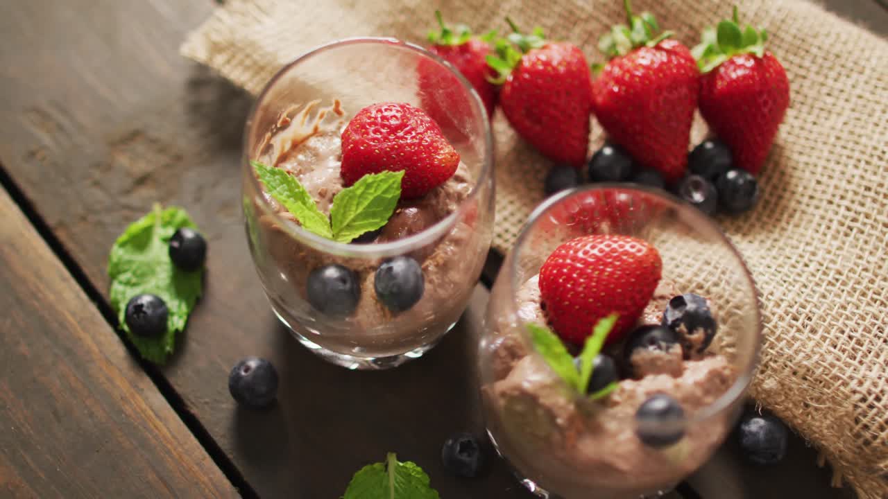 Video di budino al cioccolato con fragole e mirtilli su superficie di legno.