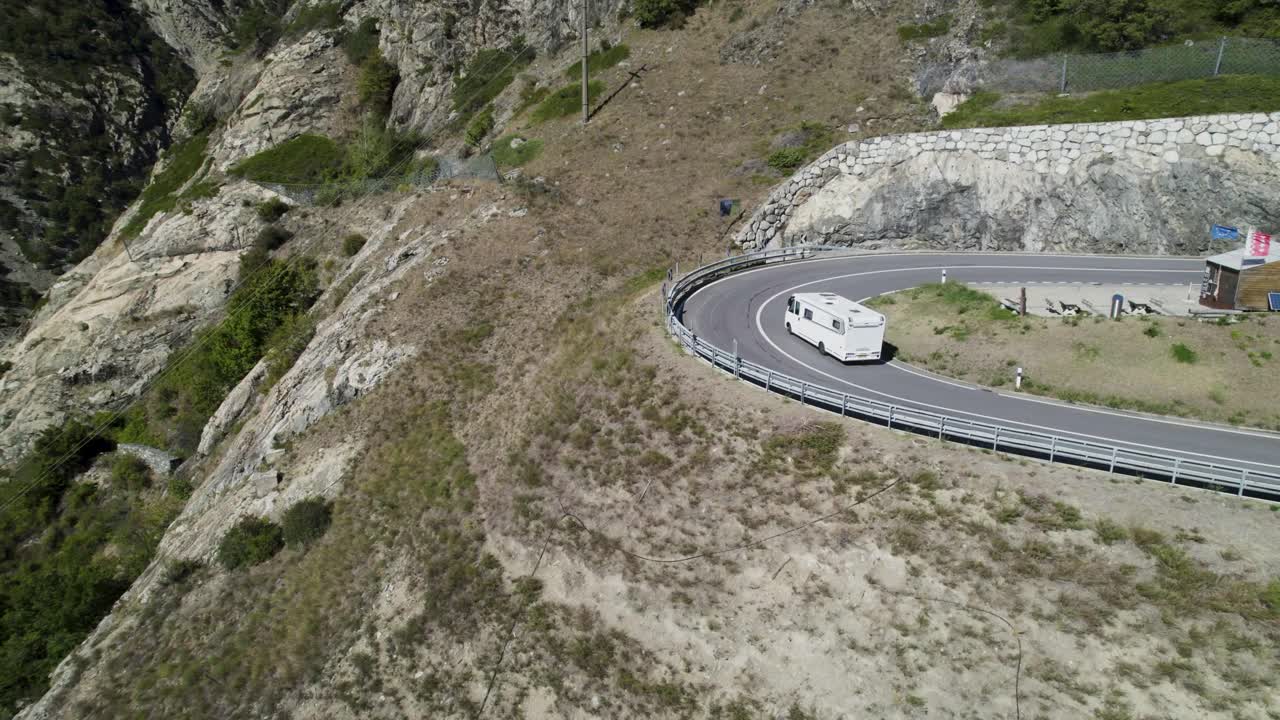 un campista navegando por una sinuosa carretera de montaña en los alpes suizos, vista aérea
