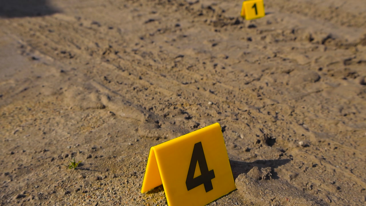 Close up view of yellow colored and numbered Crime Markers placed next to muddy tire tracks and evidenve on a mud road outdoors while sun is shining. Shallow depth of field with bokeh background.