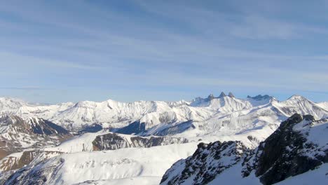 amplio droneshot de un paisaje montañoso de invierno nevado, pasando por algunas formaciones rocosas, en un día claro y soleado en los alpes franceses