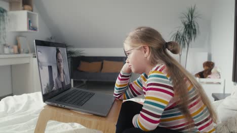 chica caucásica de edad primaria teniendo una conversación de video en una computadora portátil mientras está sentada en la cama