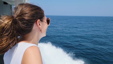 beautiful young woman in boat wearing sunglasses posing and smiling at camera while sailing in the ocean