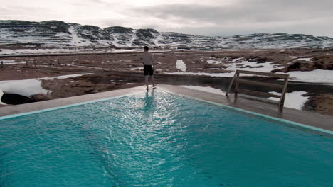 young man emerging from warm swimming pool, countryside scenery