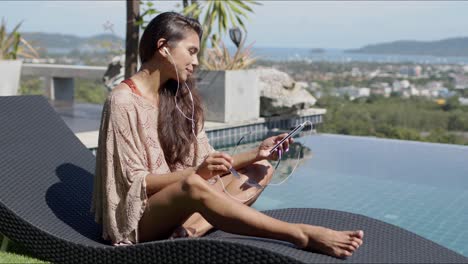 mujer relajada con teléfono inteligente escuchando música junto a la piscina