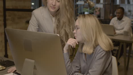 two female employees looking something at computer and talking together in the office 2