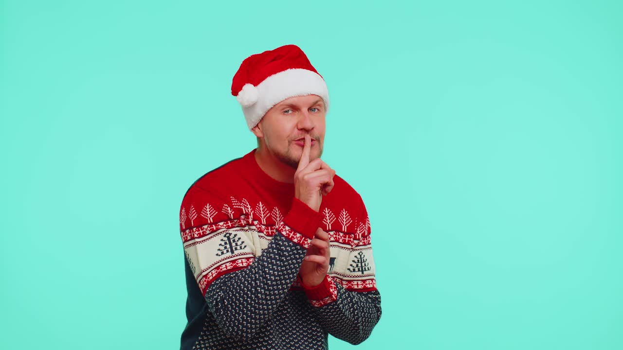 赤いクリスマスセーターを着た男性指差し指を唇に押し静けさを示すジェスチャーシグナル秘密
