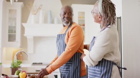 Fröhliches-Afroamerikanisches-Seniorenpaar-In-Schürzen,-Das-Essen-In-Der-Küche-Zubereitet,-Zeitlupe