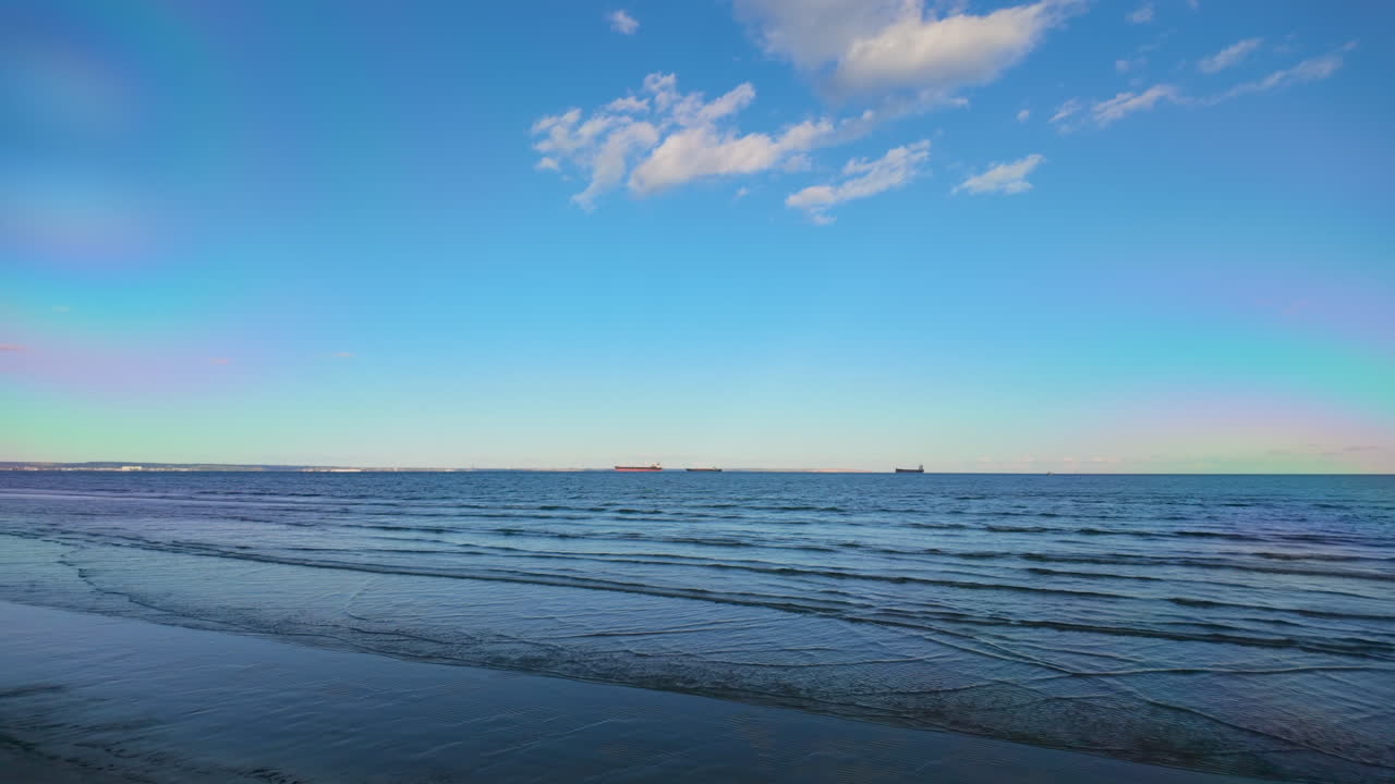 은 파란 하늘 아래 해안에 부히는 부드러운 파도와 함께 조용한 해변 장면