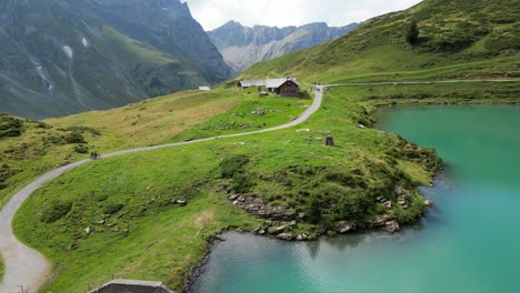 drone view of the shore of an alpine calm water lake, biking path and rocky mountains, engelberg, obwalden