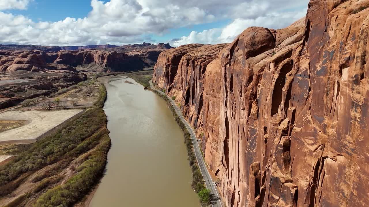 Potash Road in Moab, Utah. Close up of High Rising Red Cliffs on side of highway. Colorado River, Partly Cloudy Sky