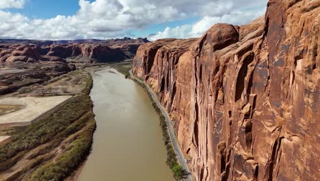potash road in moab, utah. close up of high rising red cliffs on side of highway. colorado river, partly cloudy sky