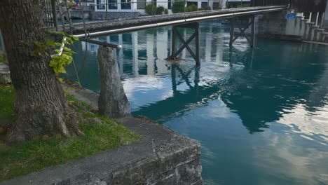 Interlaken-Immersive-POV:-Bewegung-Durch-Die-Straßen-Der-Stadt-Am-Frühen-Morgen-In-Der-Schweiz,-In-Europa,-Zu-Fuß-|-Wackelige-Dramatische-Enthüllung-Von-Der-Kleinen-Brücke-Zum-Türkisfarbenen-Wasser