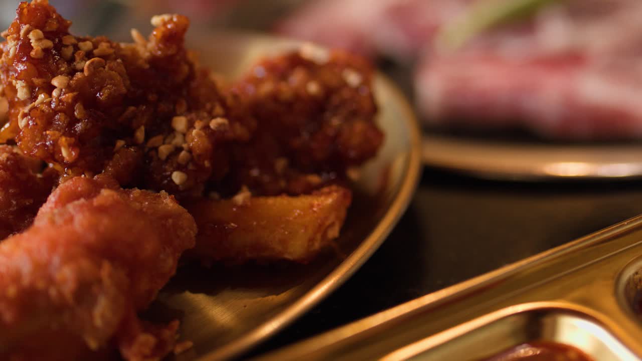 Hand places crispy fried chicken beside metal tray of sauces, sliced meat visible in background