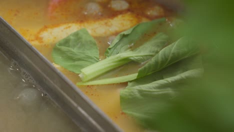 cocinar y agregar hojas frescas de bok choy en la sopa de tom yum hirviendo, comida asiática tailandesa