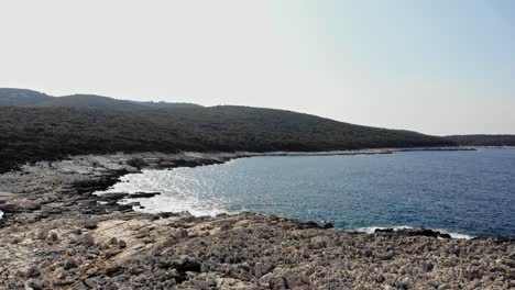 Stony-Beach-Shoreline-Of-Paralia-Emplisi-In-Kefalonia,-Greece-And-Dense-Forest-Hills-On-The-Background--Aerial