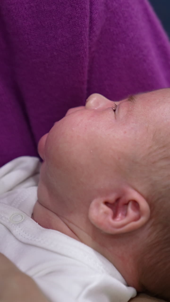 Little baby opens its mouth in hunger. Mother gives a bottle to her child, it suckles and milk drops appear on its cheek. Close up. Vertical video
