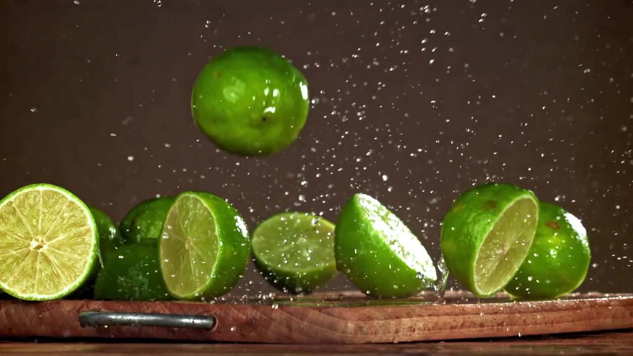 Friske limefrugter og vand, der sprøjter ned på et træbræt i slowmotion