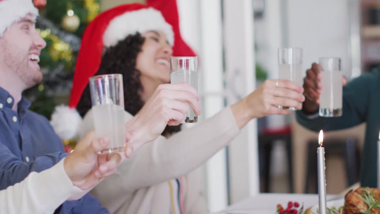 Happy group of diverse friends in santa hats celebrating meal, toasting with vine at christmas time