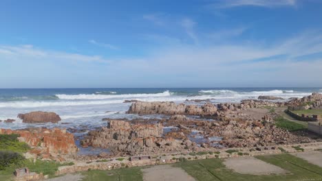 aerial drone moves from land to rocky coastline as waves crash against the shore