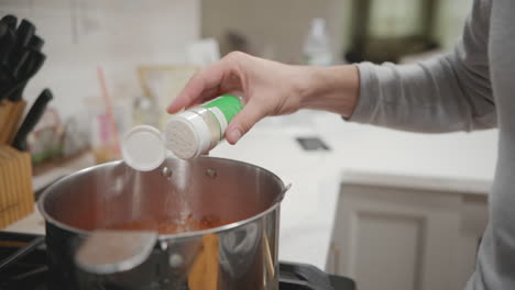 a person hand sprinking some seasoning inside a pot on a stove in slow motion, close up static