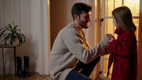 father helping daughter get dressed in a red coat